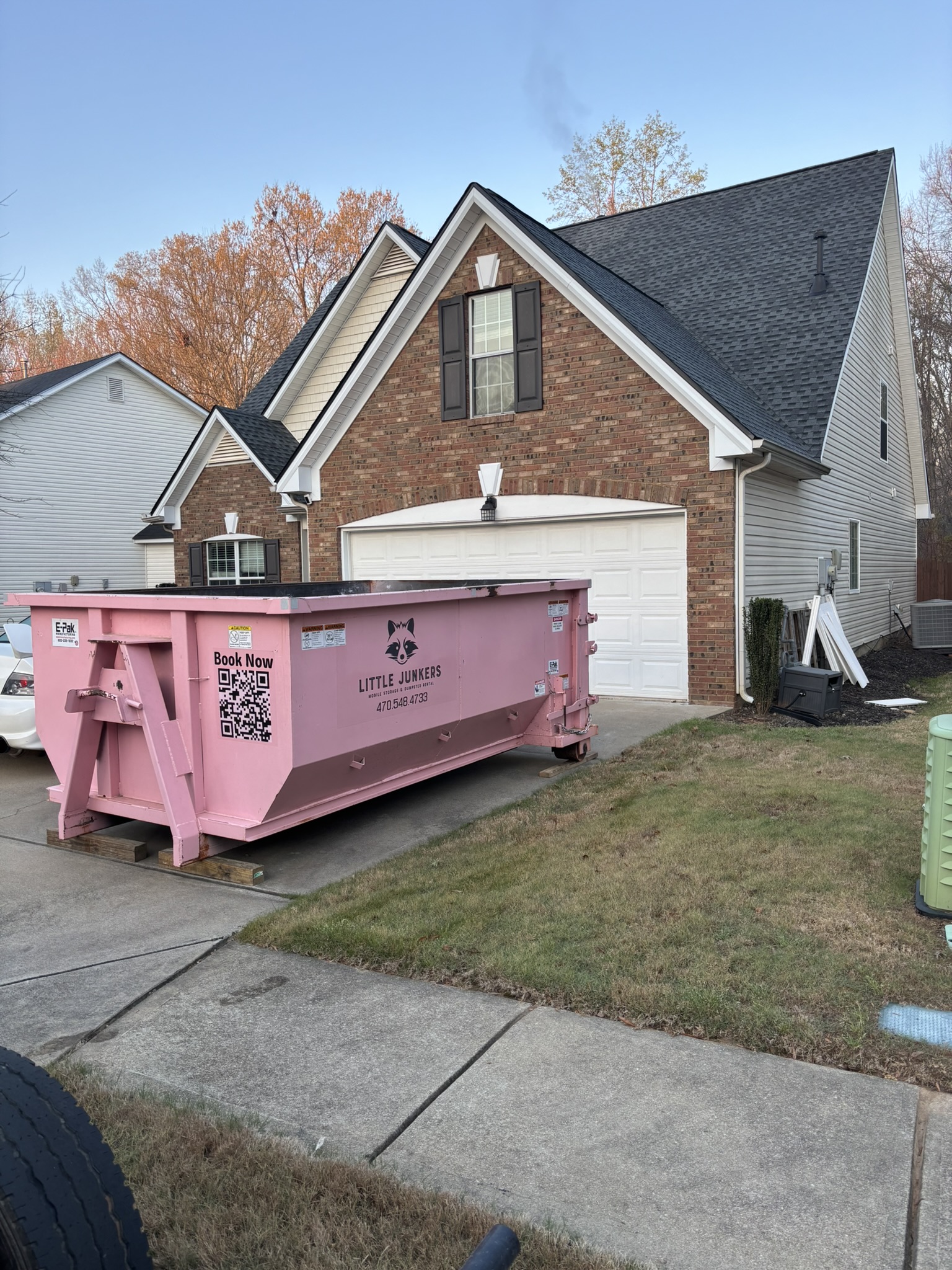 Pink 11-yard Little Junker containing wood beside a residential garage